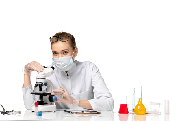 疾病前视图：女医生穿着医疗服 戴着面罩 在浅白色空间使用显微镜使用办公室显微镜