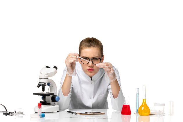 医疗前视图穿着医疗服的女医生戴着手套在白色办公桌上处理解决方案解决方案套装护目镜