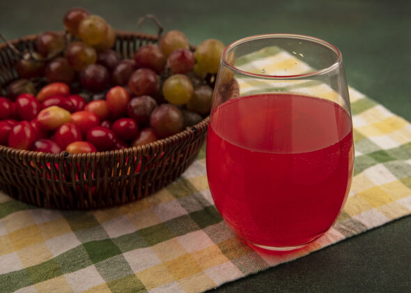 新鲜顶视图新鲜的山茱萸樱桃桶在一个格子布葡萄与新鲜果汁在一个绿色的表面玻璃果汁樱桃葡萄