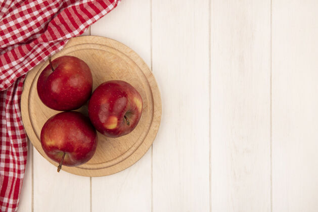 特写红色格子布上的木制厨房板上的红苹果俯视图 白色木质表面上有复印空间水果厨房健康