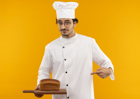 拿着年轻的男厨师穿着厨师制服 拿着眼镜 指着砧板上的面包点面包厨师