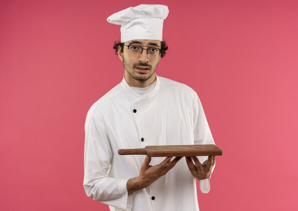 粉红年轻的男厨师穿着厨师制服 戴着眼镜拿着砧板穿厨师烹饪