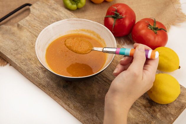 配料俯视图中的女性手拿着一个盛着扁豆汤的汤匙 汤匙放在一个木制的厨房板上 汤匙放在一块布袋上 柠檬和西红柿被隔离在一个白色的表面上健康木头持有