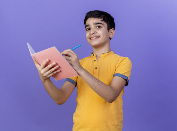 年轻人带着微笑的年轻白人男孩拿着笔记本和铅笔孤立地放在紫色的墙上 留着复印空间便笺手势铅笔