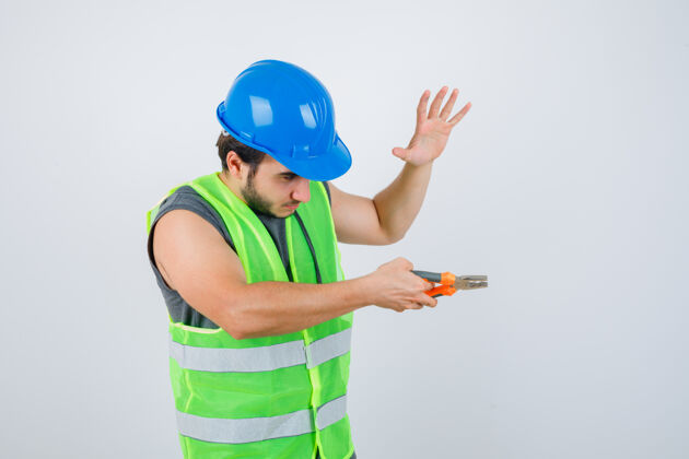 提高年轻的建筑工人手拿钳子 手举手掌 穿着工作服 看上去很自信正视图酷前面胡须