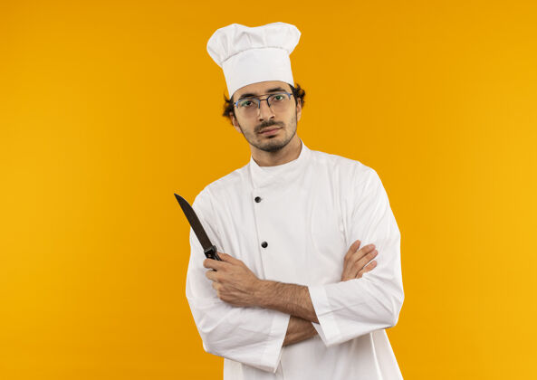 信心自信的年轻男厨师穿着厨师制服 戴着眼镜 双手交叉 手持刀眼镜男性厨师