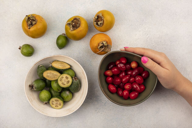 柿子女性手拿着一碗凤梨樱桃的俯视图 碗上有飞珠 柿子孤立在灰色的表面上飞珠碗营养