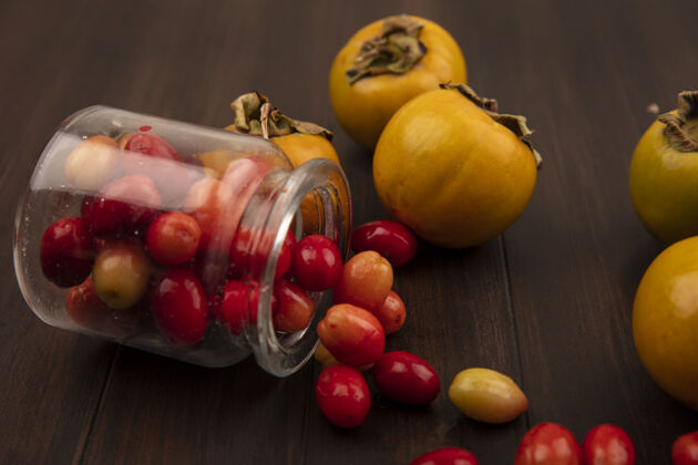 美味从玻璃罐中掉落的红色茱萸樱桃俯视图 柿子果实被隔离在木制表面上健康营养罐子