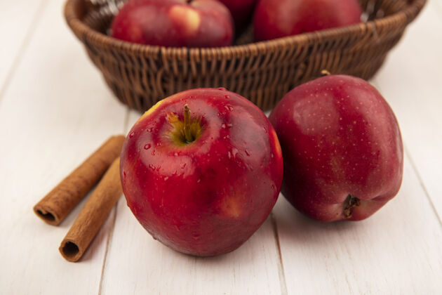 食品顶视图是一个红色的苹果 苹果放在一个桶里 肉桂枝孤立在一个白色的木制表面上苹果营养棒