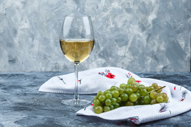 毛巾一些绿色的葡萄和一杯葡萄酒在肮脏的石膏和厨房毛巾的背景下 侧视图葡萄酒水果食物