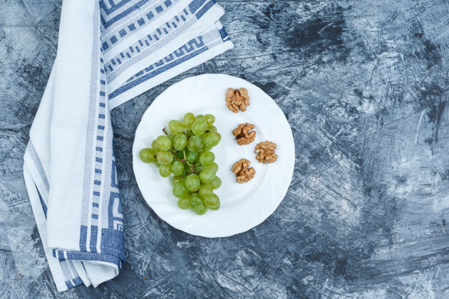 树叶平铺白葡萄 核桃在白色盘子里 厨房毛巾在深蓝色大理石背景上水平酒庄有机浆果