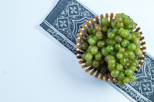 美味绿色的葡萄在一个篮子里平放在白色和厨房毛巾的背景上卷须有机秋天