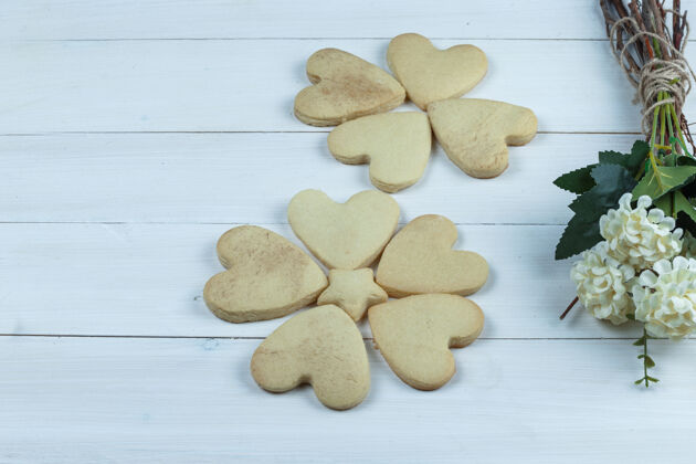 脆白色木板背景上的一组鲜花和心形饼干特写脆堆甜点