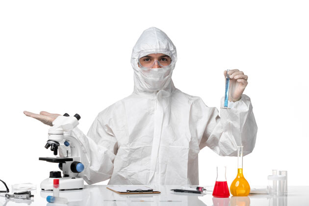 大流行正面图：男医生穿着防护服 戴着口罩 因为白色空间上有一个装有蓝色溶液的瓶子医生溶液到期