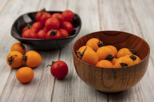 农业木制碗上的橙色西红柿与灰色木制表面上的黑色碗上的红色西红柿的顶视图新鲜营养配料