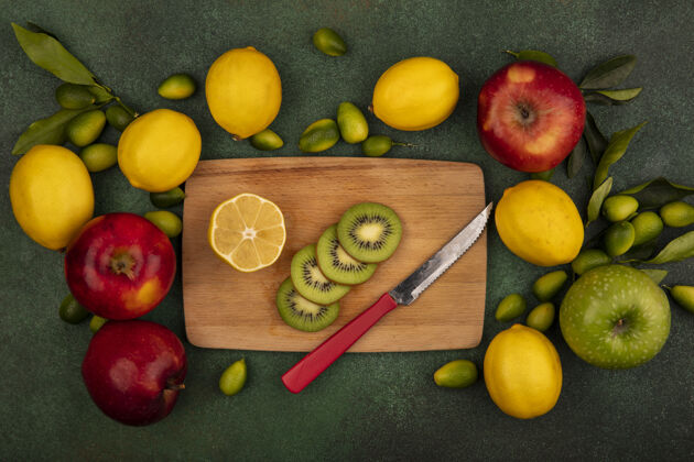 多汁木制菜板上猕猴桃切片的俯视图 刀子上有柠檬和五颜六色的苹果 它们被隔离在绿色的表面上苹果自然成熟