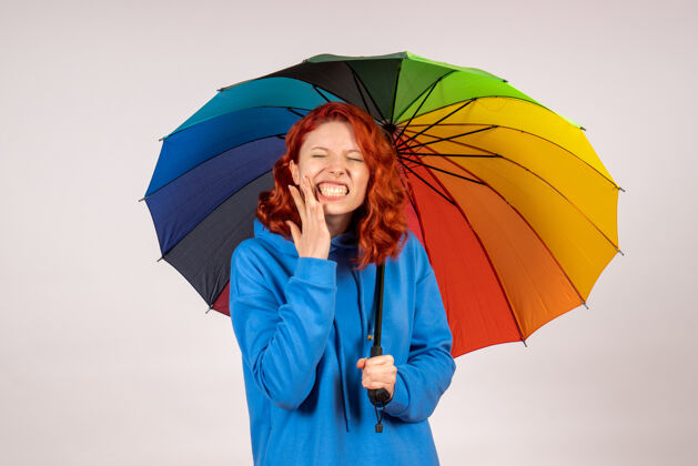 前面白色墙壁上带着彩色雨伞的年轻女性的正视图庇护所保护掩护情绪