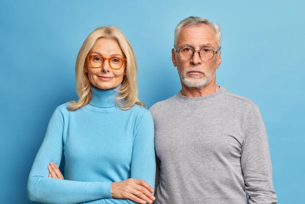 老年人老年夫妇的画像退休老人们穿着休闲服 戴着眼镜 紧紧地站在一起 享受在一起的甜蜜时光 或是在蓝色的墙壁上与世隔绝的退休时光头发光关怀