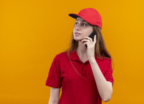 年轻穿着红色制服的年轻送货女孩在电话里说话 看着隔离的橙色墙上的左边 还有复印空间侧线送货左边