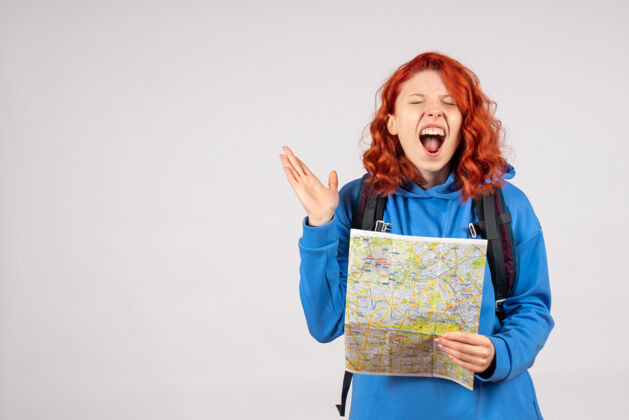 旅行年轻女性的正面图 白色墙上有背包和地图漂亮前面人