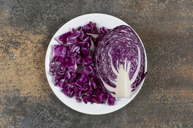 可口半片红心菜旁边切碎的白菜 放在盘子上 放在大理石表面有机的健康的成熟