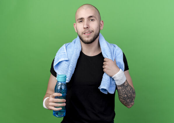 年轻喜欢运动的年轻人戴着手环 肩上扛着毛巾的水瓶 隔离在绿色的墙上奶瓶运动型请穿