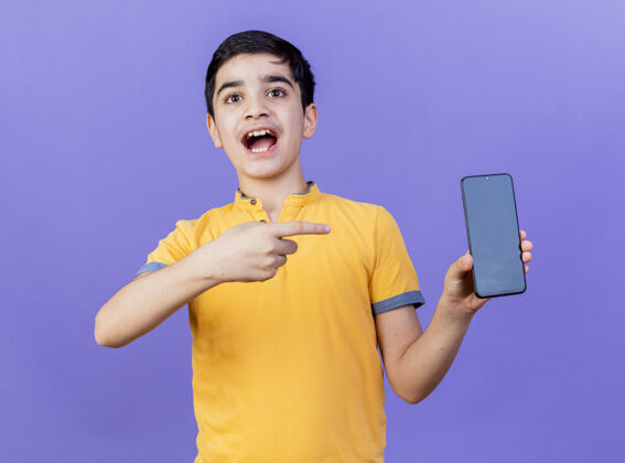 显示令人印象深刻的年轻白人男孩显示和指着手机孤立在紫色墙上表达电话印象