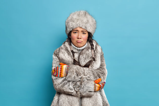 脸不幸的斯堪的纳维亚妇女戴着毛皮帽子和外套 双手交叉 在严寒的天气里穿着冬季外套 感到冻僵发抖姿势北极人