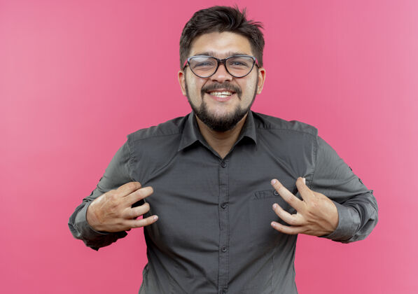 年轻人面带微笑的年轻商人戴着眼镜拿着隔离在粉红色墙上的衬衫拿着眼镜微笑