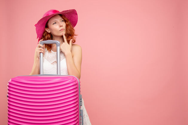 包年轻的女性游客与粉红色的帽子和粉红色的墙壁上的包的正面视图帽子漂亮情感