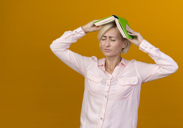 讨厌一个年轻的金发斯拉夫女人闭着眼睛 头上盖着一本书 孤零零地贴在橙色的墙上金发年轻封闭