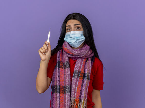 年轻焦急的年轻白种人病女孩戴着面具和围巾拿着温度计隔离在紫色的墙上 留着复印空间焦虑疾病体温计