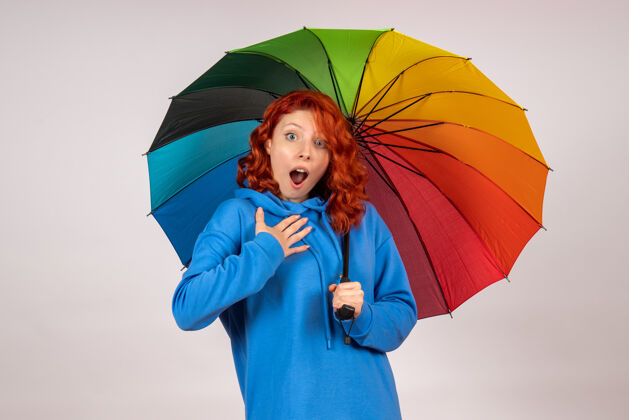 天气白色墙壁上带着彩色雨伞的年轻女性的正视图保护伞空气