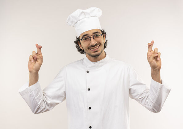 厨师面带微笑的年轻男厨师身穿厨师制服 戴着眼镜 手指交叉 孤立在白墙上穿眼镜烹饪