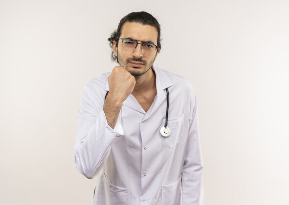 年轻严格的年轻男性医生 戴着眼镜 穿着白色长袍 手持听诊器 在隔离的白色墙壁上举起拳头 留有复印空间穿男性提高