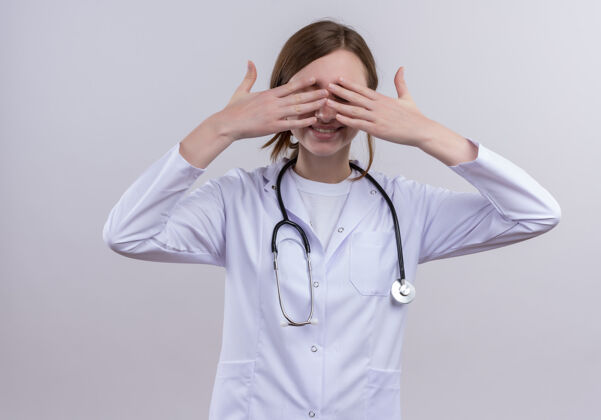 听诊器面带微笑的年轻女医生 穿着医用长袍 戴着听诊器 双手紧闭双眼 站在隔离的白墙上封闭女士医疗