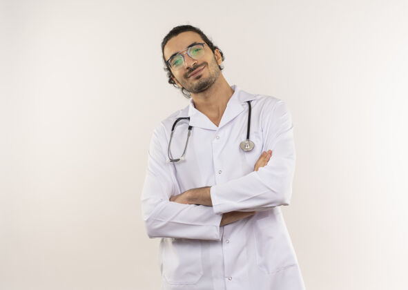听诊器年轻的男医生戴着眼镜 穿着白色长袍 听诊器 双手交叉放在隔离的白墙上 留着复印空间十字架戴医生