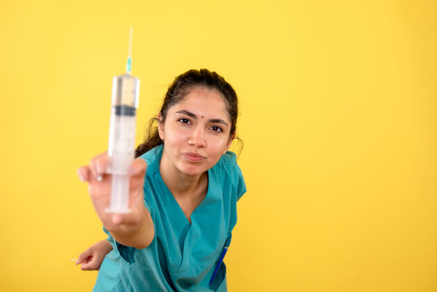 工作年轻女医生在黄色隔离墙上展示注射器的前视图微笑成人医生