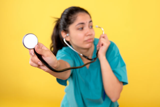 健康黄色隔离墙上带听诊器的年轻女医生的正面图人年轻女医生快乐