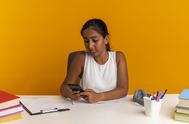 坐着年轻的女学生坐在书桌旁 手里拿着学习工具 看着橘色墙上的电话抱着工具书桌