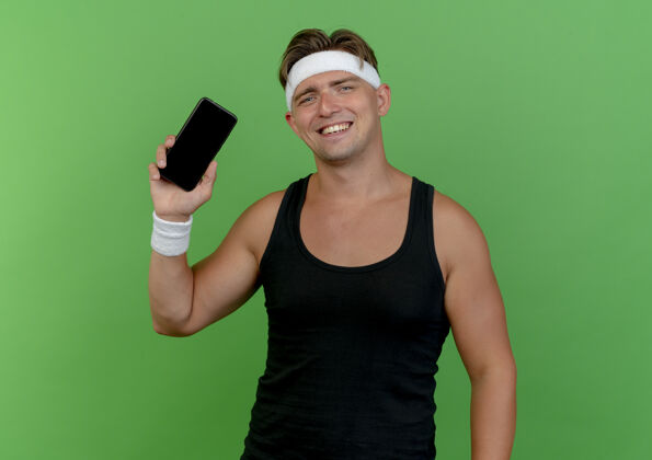 绿色快乐微笑的年轻帅气运动男戴着头带和腕带显示手机绿色隔离腕带微笑佩戴
