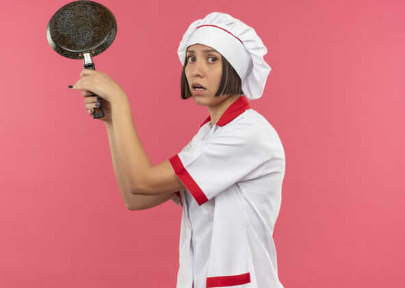 锅令人印象深刻的年轻女厨师在厨师制服举行炒锅上粉红色的复制空间隔离厨师女制服