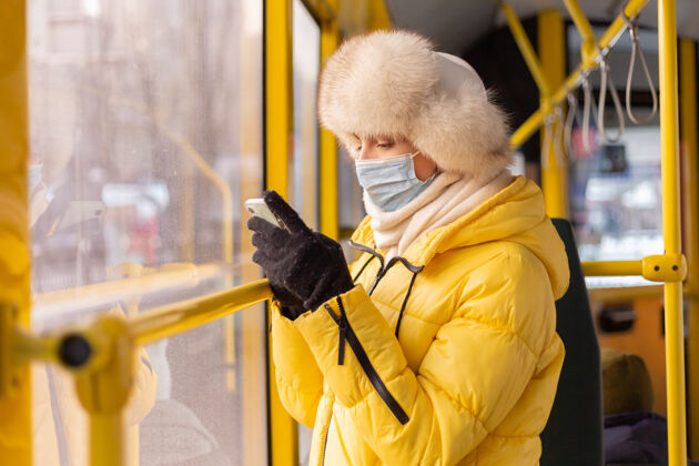 乘客一幅阳光明媚的肖像画 描绘了一个冬天 穿着暖和衣服 手里拿着手机 坐在城市公共汽车上的年轻女子时尚公共汽车过境