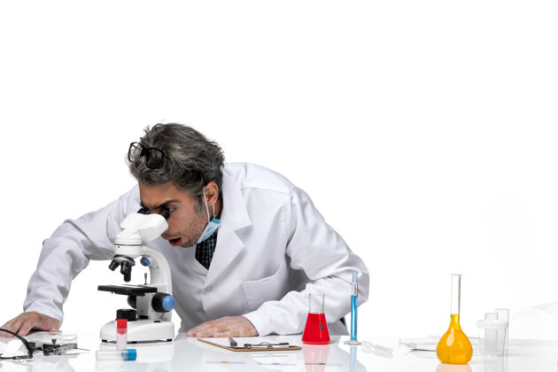 视图前视图中年科学家穿着特殊的白色西装使用显微镜办公桌科学使用