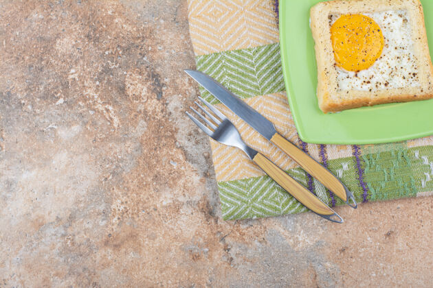 面包在绿色盘子上放上带香料的鸡蛋吐司 还有餐具和桌布美味面包房餐具