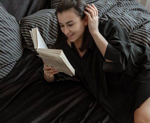 阅读穿着睡衣的漂亮年轻女子躺在床上看书特写家常独处