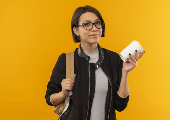 空间自信的年轻女学生戴着眼镜 背着袋子拿着咖啡杯 孤立地放在橙色的空间里自信包学生