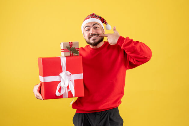 快乐黄色背景下手持圣诞礼物的年轻男性正面图快乐微笑年轻男性