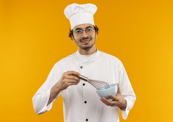 制服面带微笑的年轻男厨师 身穿厨师制服 戴着眼镜 拿着威士忌和碗 隔离在黄色的墙上男性微笑年轻