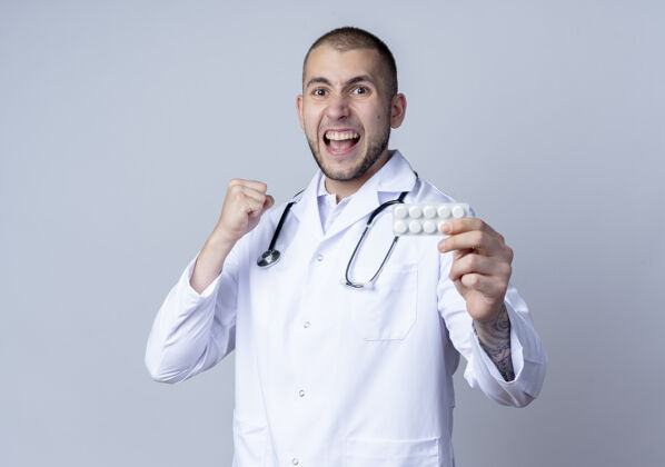 医疗自信的年轻男医生 穿着医用长袍 脖子上戴着听诊器 手里拿着一包药片 紧握着白色的拳头周围男性信心